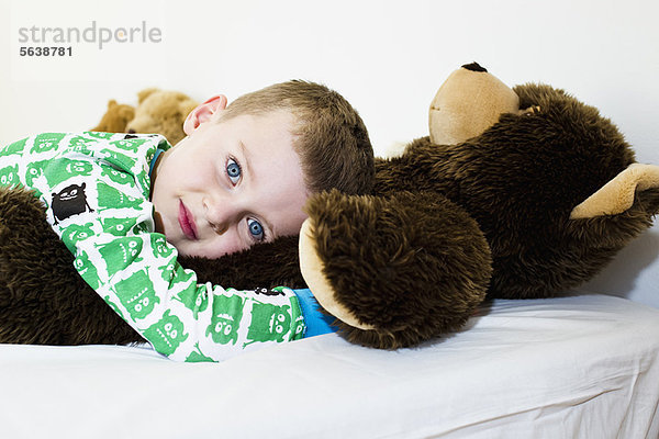 Junge umarmender Teddybär im Bett