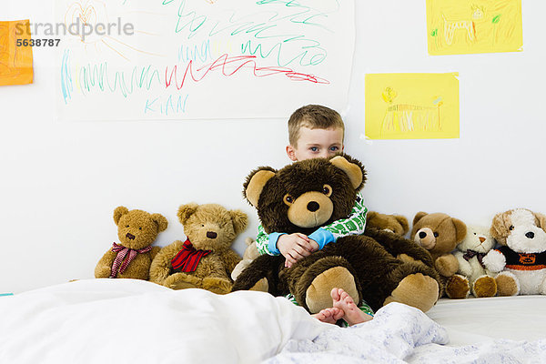 Junge umarmender Teddybär auf dem Bett