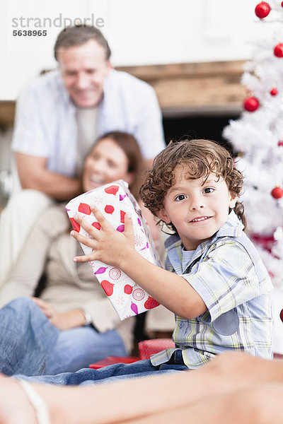 Junge schüttelt verpacktes Weihnachtsgeschenk