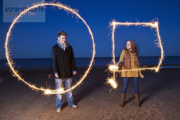 Pärchen spielen mit Wunderkerzen am Strand