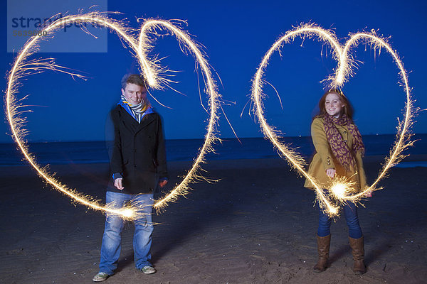 Pärchen spielen mit Wunderkerzen am Strand