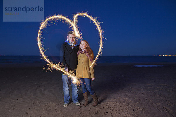 Pärchen spielen mit Wunderkerzen am Strand