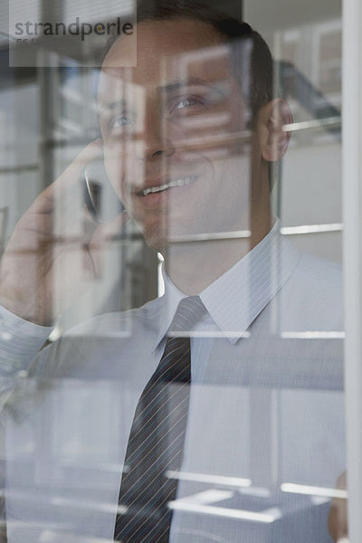 Ein Geschäftsmann im Gespräch mit einem Handy  durchs Fenster gesehen