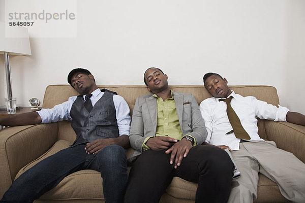 Drei erschöpfte Freunde schlafen auf einem Sofa.