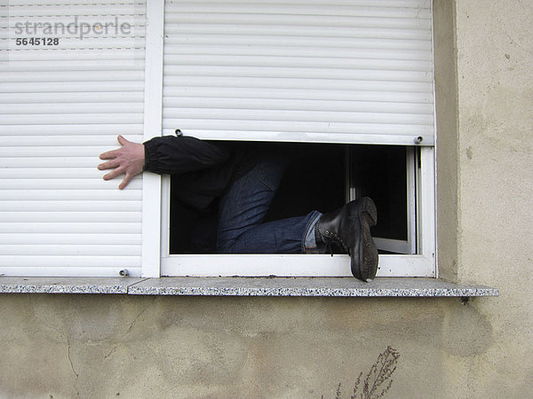 Ein Mann  der durch ein Fenster klettert.
