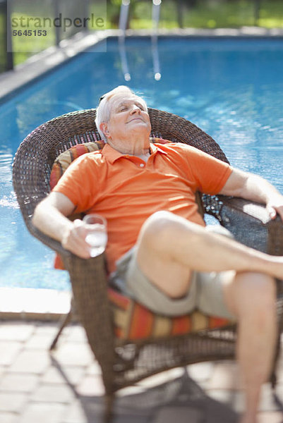 Ein pensionierter älterer Mann  der sich in der Sonne neben einem Pool entspannt.