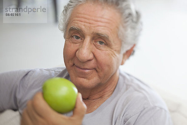 Ein älterer Mann  der sich darauf vorbereitet  einen grünen Apfel zu essen.