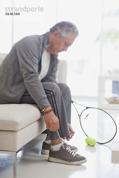 Ein älterer Mann  der seine Schnürsenkel bindet und sich darauf vorbereitet  Tennis zu spielen.