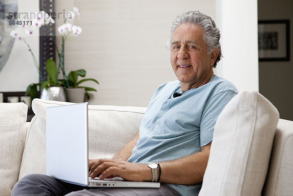 Ein fröhlicher älterer Mann mit einem Laptop zu Hause