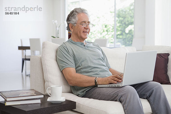 Ein älterer Mann  der zu Hause einen Laptop benutzt.