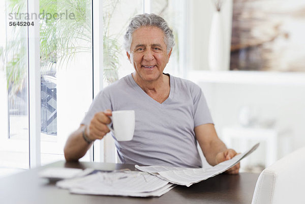 Ein fröhlicher älterer Mann  der die Zeitung liest und Kaffee trinkt.