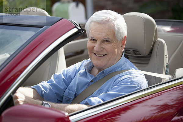 Ein fröhlicher älterer Mann  der einen Cabrio-Sportwagen fährt.