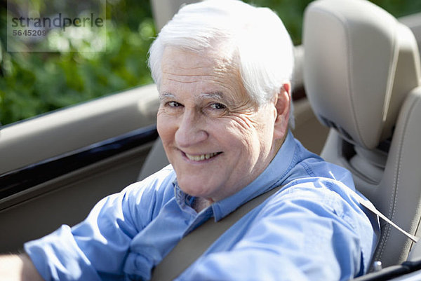 Ein fröhlicher älterer Mann  der einen Cabrio-Sportwagen fährt.