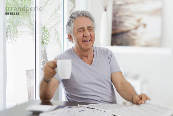 Ein fröhlicher Senior mit einer Tasse Kaffee und einer Zeitung.