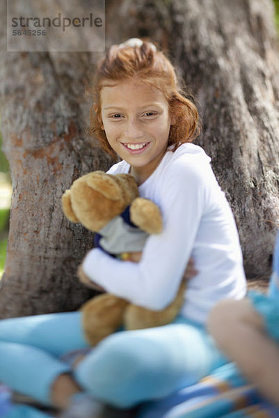 Mädchen umarmender Teddy neben Baum