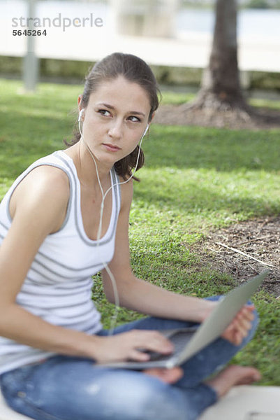 Mädchen mit gekreuzten Beinen im Park mit Laptop