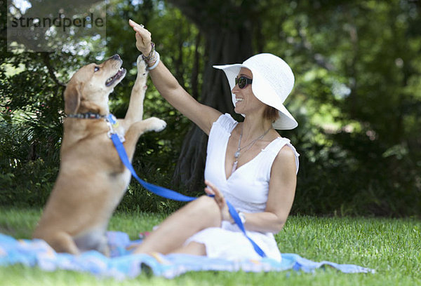 Gut gekleidete Frau spielt mit ihrem Hund im Park