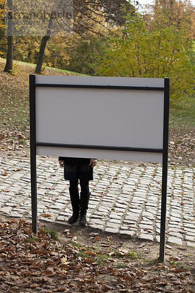 Eine Frau  die hinter einem Schild in einem Park steht.