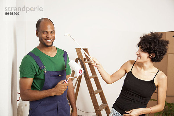 Ein verspieltes Paar mit Spaß beim Malen der Wohnung