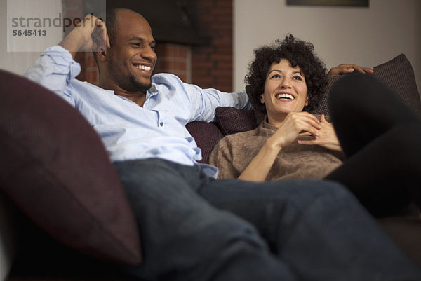 Ein lachendes Paar  das sich gemeinsam auf einem Sofa ausruht.