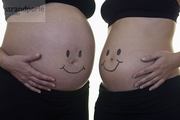 Zwei schwangere Frauen mit Smiley-Gesichtern auf dem Bauch  Mittelteil