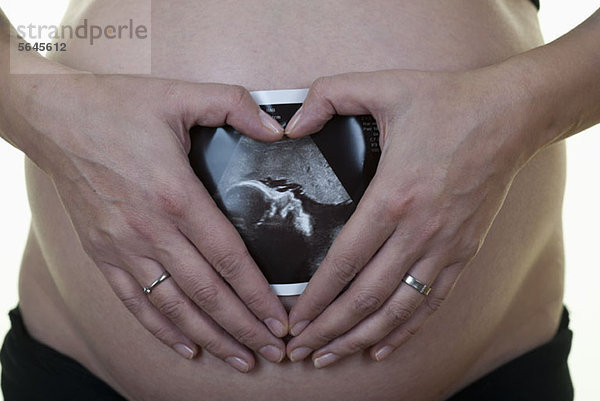 Eine schwangere Frau  die einen Ultraschallausdruck gegen ihren Bauch hält.