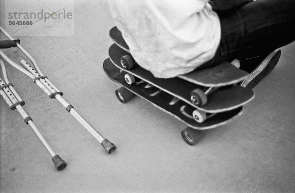 Ein Mann sitzt auf einem Stapel Skateboards neben Krücken.