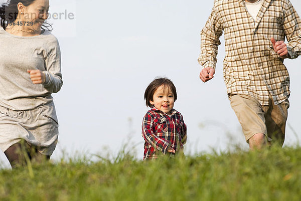 Ein kleiner Junge  der im Park zwischen seiner Mutter und seinem Vater rennt.
