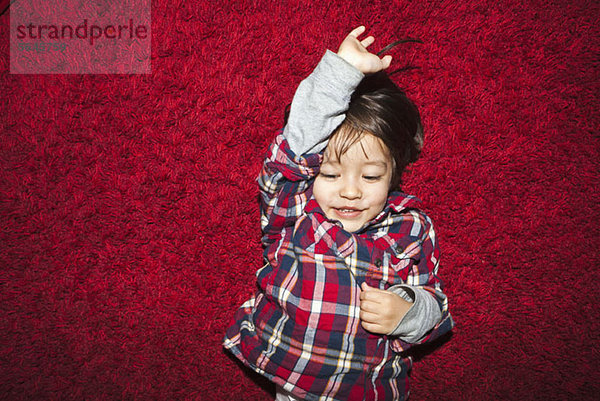 Ein junger lächelnder Junge liegt auf einem roten Teppich.