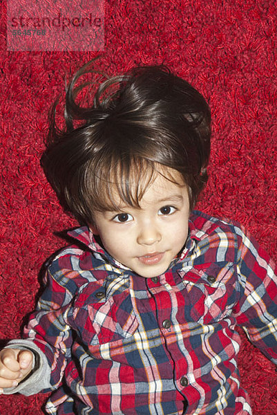 Ein kleiner Junge  der auf einem roten Teppich liegt.