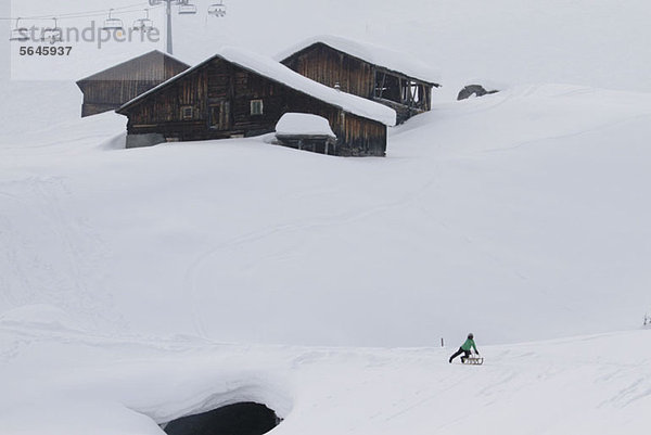 Kind auf Schlitten unter Blockhütten auf schneebedecktem Hügel