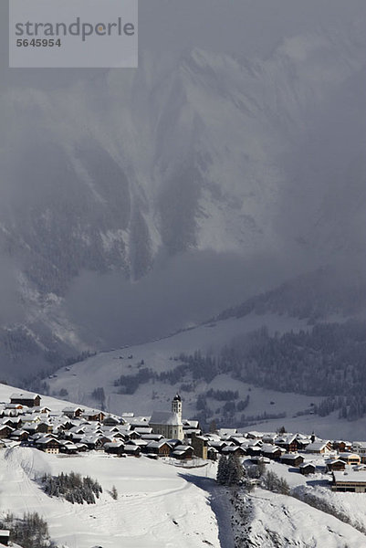 Verschneites Dorf mit Bergkette und Tal im Hintergrund