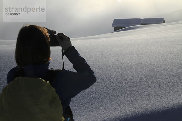 Wanderer fotografiert schneebedeckte Blockhütten in der Ferne