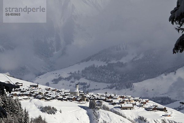 Verschneites Dorf mit Bergkette und Tal im Hintergrund