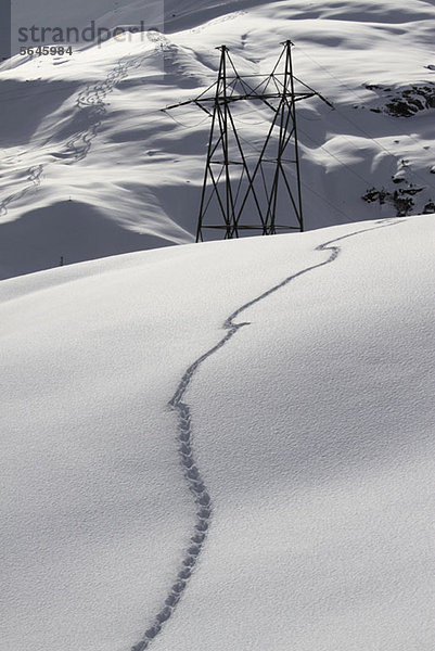 Schneefußabdrücke auf dem Hügel mit elektrischem Pylon im Hintergrund