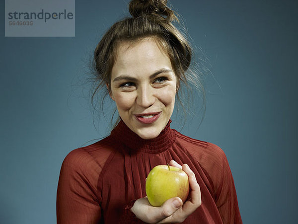 Eine hippe junge Frau hält einen Apfel und lächelt