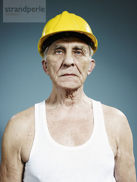 Ein ernster älterer Mann  der einen Schutzhelm und ein Tank-Top trägt.