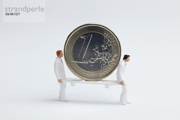 Miniatur-Sanitäterfiguren mit einer Euro-Münze auf einer Trage