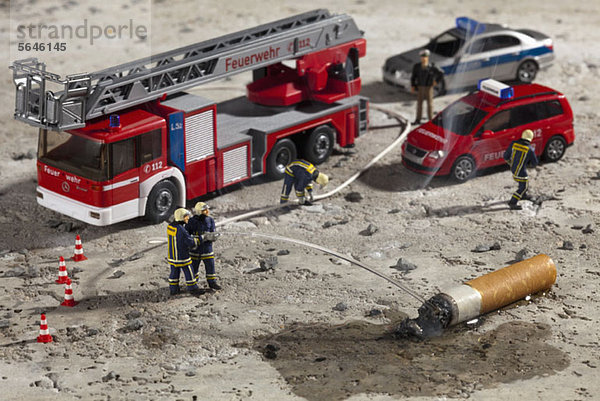 Miniaturfiguren von Feuerwehrmännern  die mit einem Schlauch einen rauchenden Zigarettenstummel ausstoßen