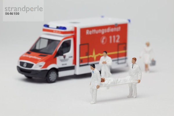 Miniatur-Sanitäterfiguren  die einen Patienten auf einer Trage aus einem Spielzeugwagen tragen.