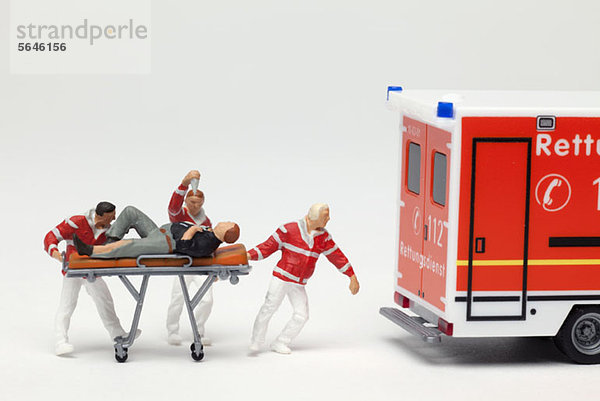 Miniatur-EMT-Figuren  die einen Patienten auf einer Trage zu einer Spielzeugambulanz bringen.