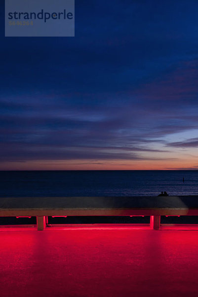 Blick auf das Meer bei Sonnenuntergang von einer beleuchteten Strandpromenade aus