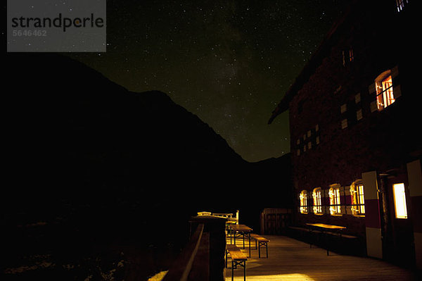 Ein beleuchtetes Gebäude gegen einen silhouettierten Berg und Sternenhimmel