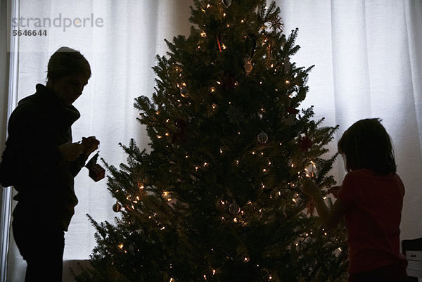 Silhouette von Mutter und Tochter beim Dekorieren eines Weihnachtsbaums