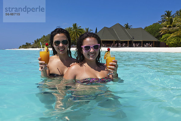 Zwei Mädchen  ca. 14 und 18 Jahre  mit Sonnenbrillen  trinken Cocktails in einer türkisfarbenen Lagune im Meer  hinten Malediveninsel Paradise Island  Lakanfinolhu  Malediven  Indischer Ozean  Asien
