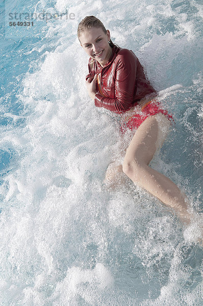 Deutschland  Nordrhein-Westfalen  Düsseldorf  Junge Frau im Schwimmbad sitzend  lächelnd  Portrait