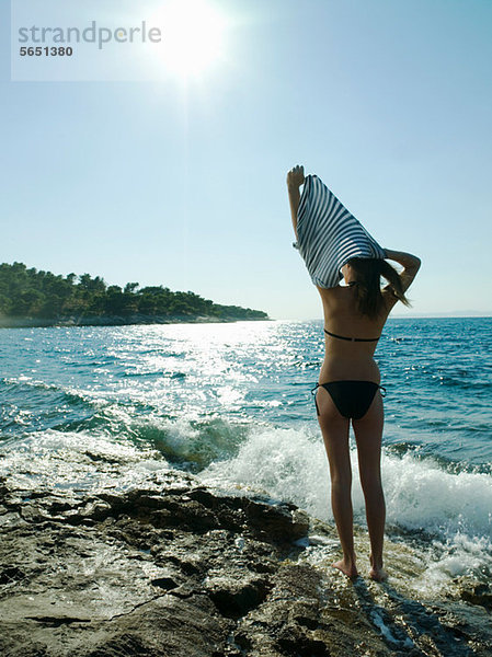 Junge Frau beim Ausziehen des T-Shirts am Meer