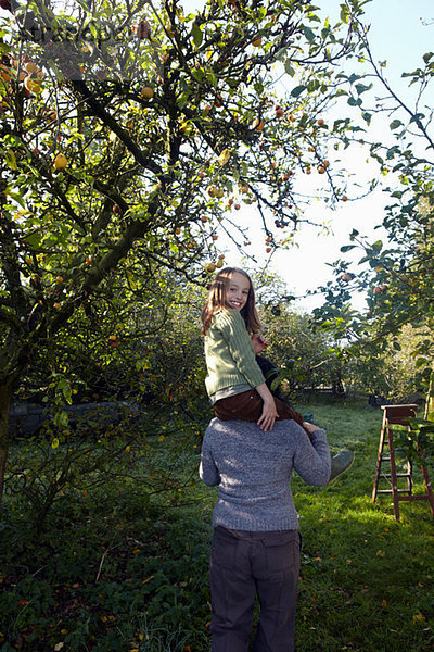 Mädchen auf der Mutter Schultern im Obstgarten