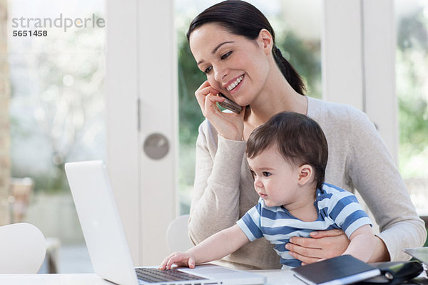 Mutter auf dem Handy und Baby beim Blick auf den Laptop