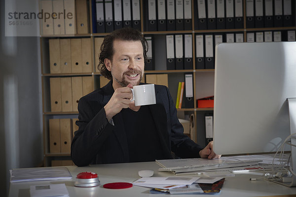Erwachsener Mann mit Kaffeetasse im Büro  lächelnd